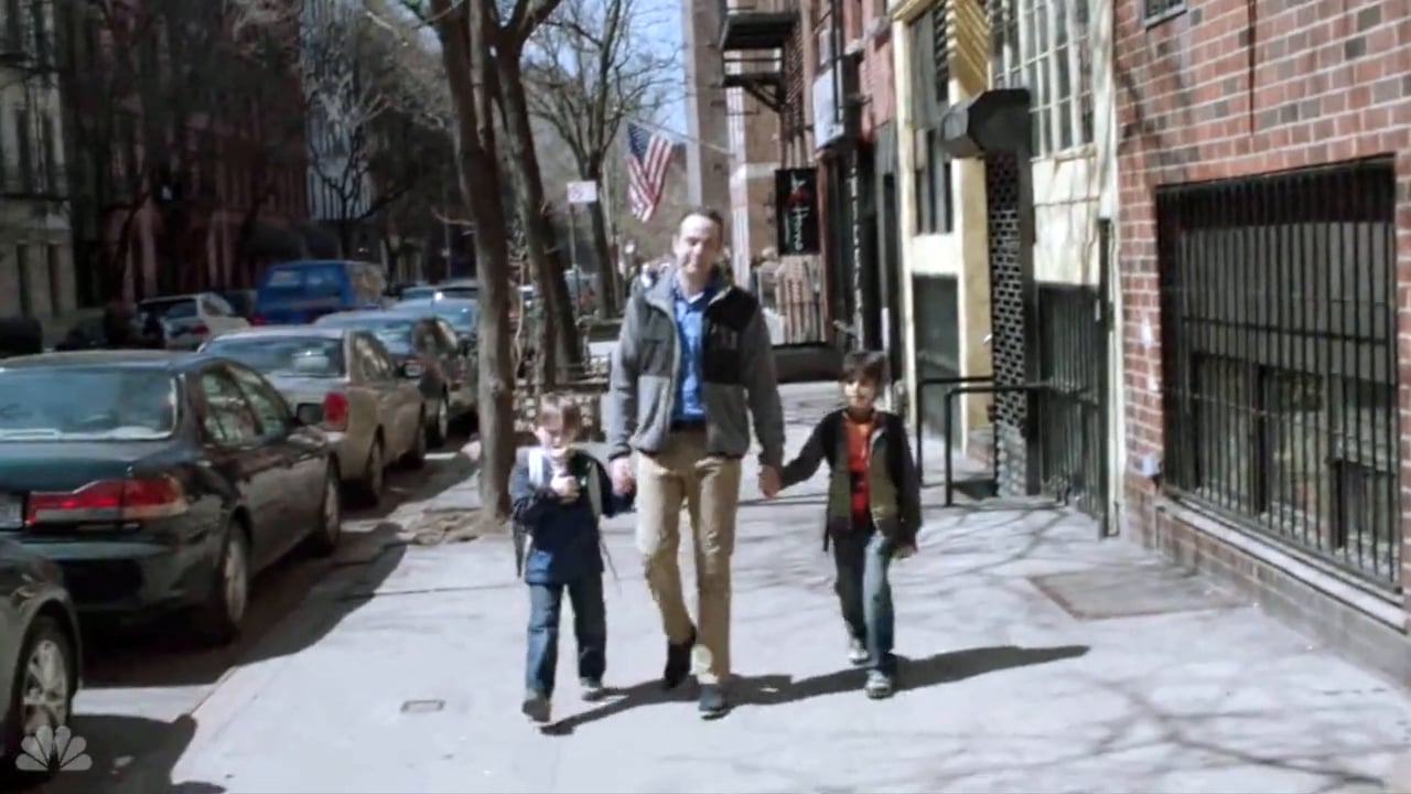 A man walks down the sidewalk holding hands with two children, one on each side.